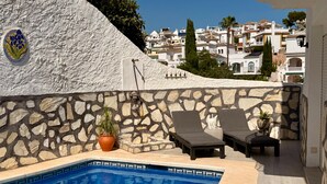 A pool area with stone walls, lounge chairs, and a view of a coastal town. - Charming Apartment in Burriana With Private Pool! (Nerja)