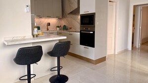 A modern kitchen with a marble countertop, two bar stools, a built-in oven, and a microwave. - Charming Apartment in Burriana With Private Pool! (Nerja)
