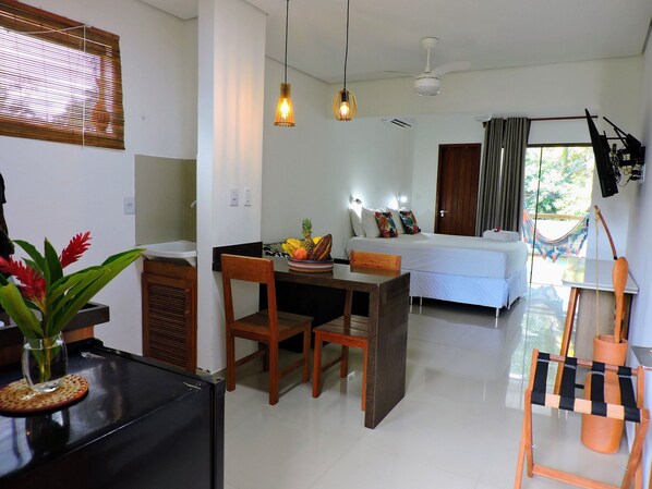 A modern hotel room with a bed, a dining area, and a kitchen.