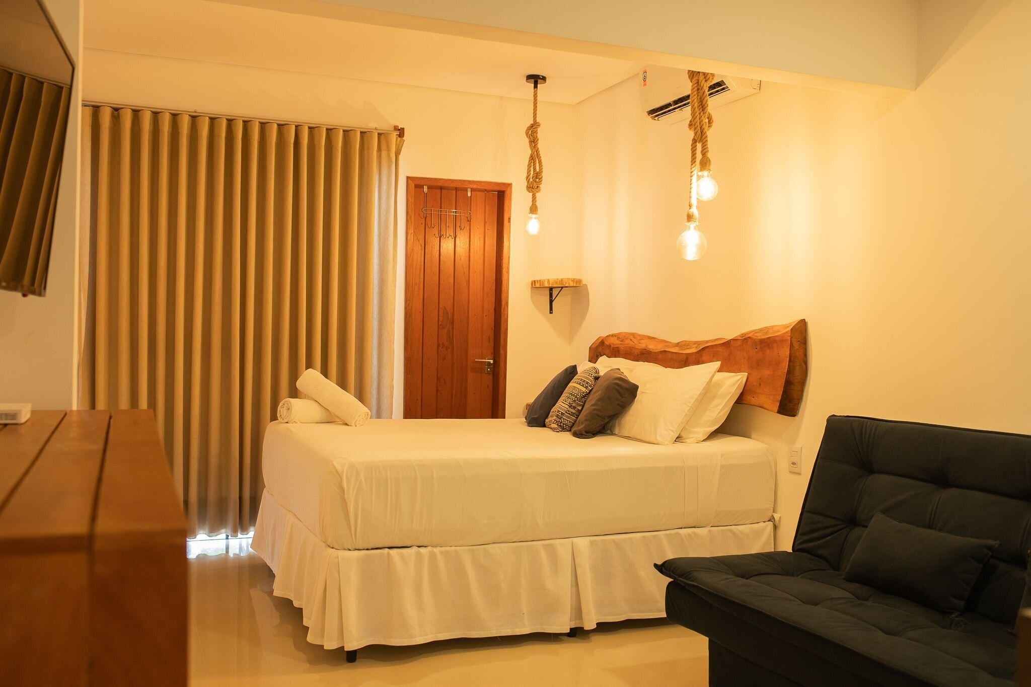 A bedroom with a bed, a wooden headboard, a black sofa, a wooden table, and a window with curtains.