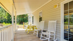 Eine Holzterrasse mit überdachter Veranda, weißen Schaukelstühlen und einem gelben Picknicktisch.