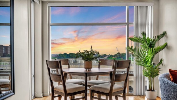 A dining area with a round table and chairs, a potted plant, and a view of a sunset over a cityscape.