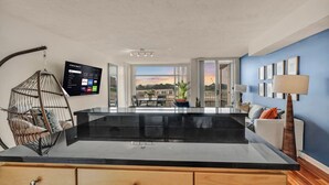 A modern kitchen with a black countertop, wooden cabinets, a hanging chair, and a view of the outside through large windows.