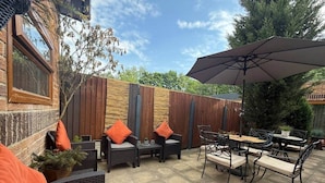 An outdoor patio with wicker furniture, a wooden fence, and a large umbrella. - Studio C - Newly renovated private 1 bed studio (Gamston)