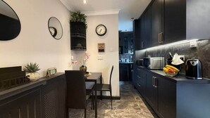 A modern kitchen with dark cabinetry, a dining area with a table and chairs, and a clock on the wall. - Studio C - Newly renovated private 1 bed studio (Gamston)