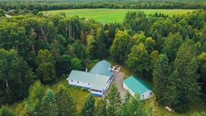 Une grande maison avec un toit végétalisé, entourée d’une forêt dense et, au loin, d’un champ verdoyant.