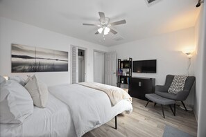A modern bedroom with a bed, a ceiling fan, a TV, and a seating area.
