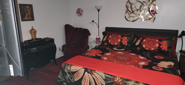 Une chambre à coucher comprenant un lit, une chaise, une table de chevet, une lampe et un élément décoratif mural.