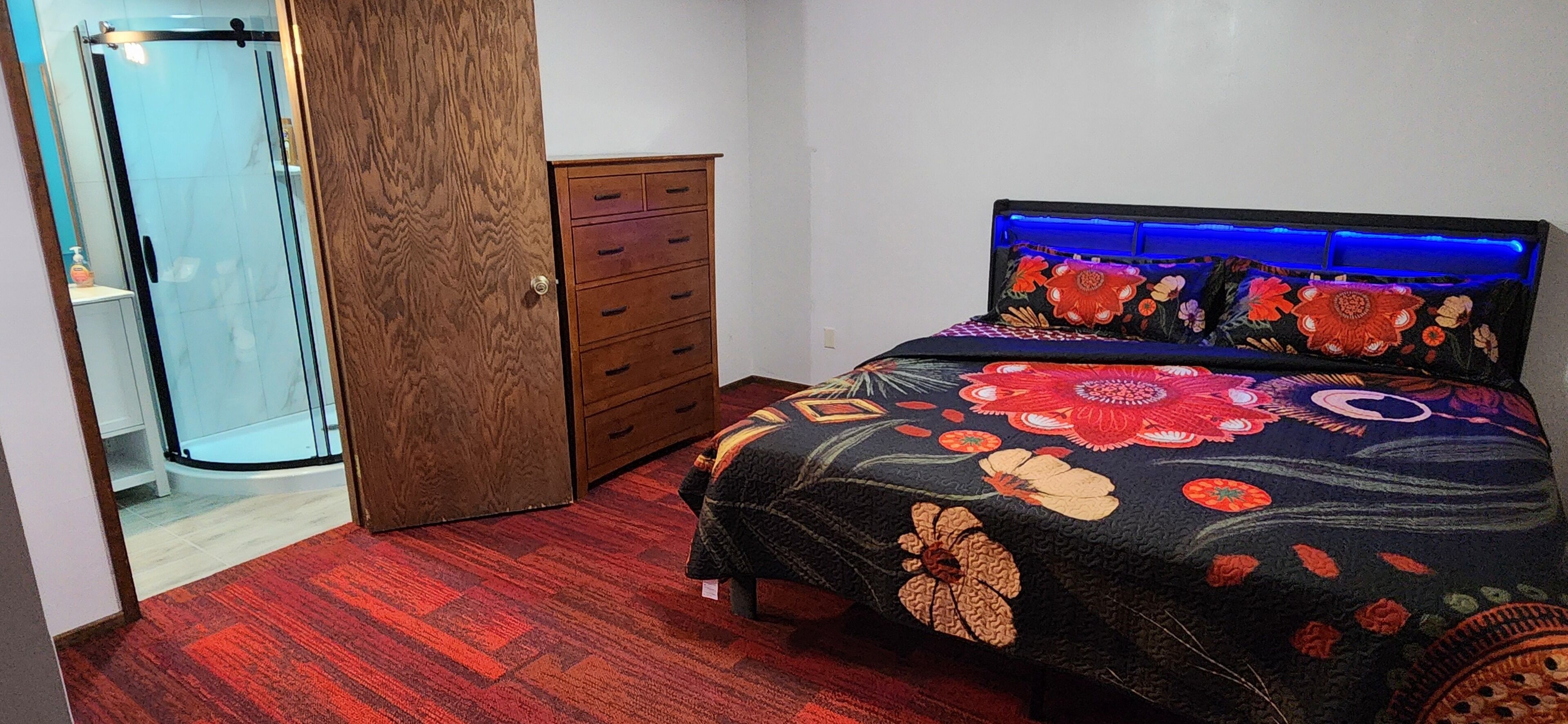 A bedroom with a glass shower door, a wooden wardrobe, and a bed with a floral bedspread.