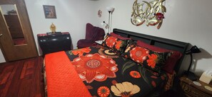 Une chambre à coucher avec un lit recouvert d’une couvre-lit à motifs floraux, une commode en bois, une chaise rouge et un élément décoratif mural.