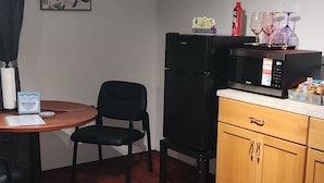 A compact room with a dining table, chairs, a black refrigerator, a wooden cabinet, and a ceiling light fixture.