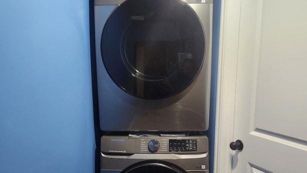 A stacked washer and dryer unit in a room with blue walls and a white door.