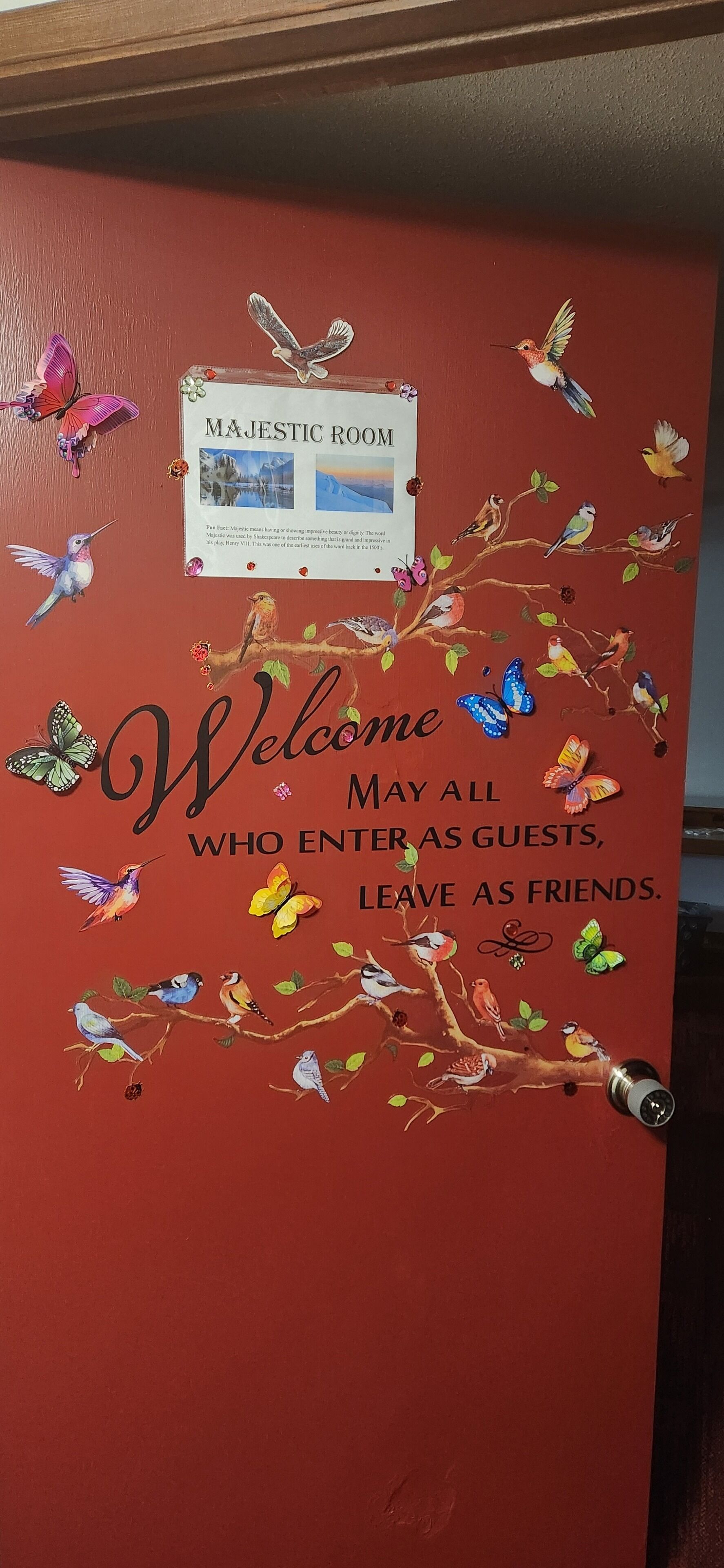 A red wall with a welcome sign and decorative birds and butterflies.