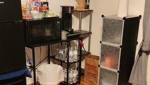 Un salon équipé d’un téléviseur à écran plat, d’une machine à café, d’un four à micro-ondes, d’une étagère avec des en-cas, d’une poubelle et d’un fauteuil.