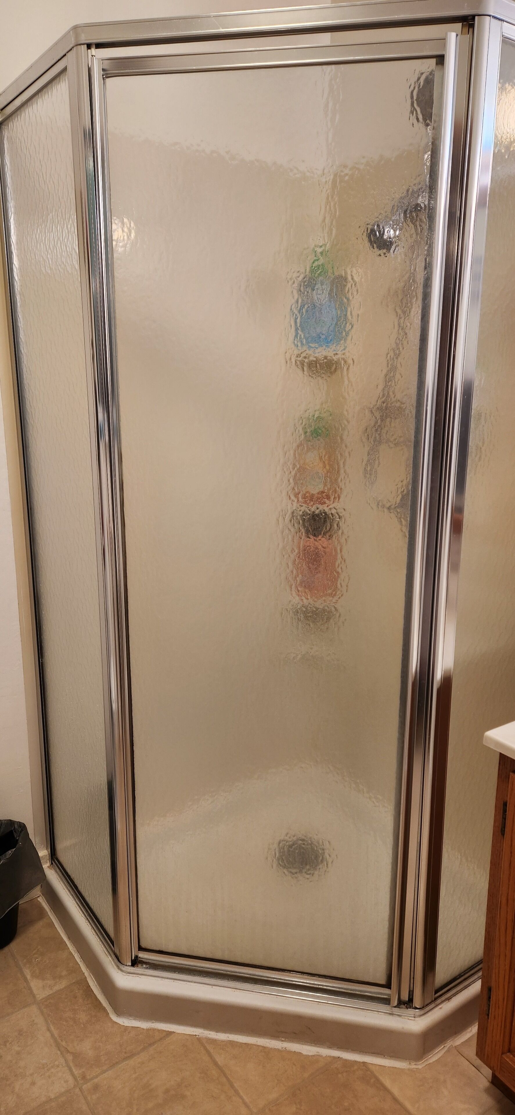 Mampara de ducha esquinera con puerta de cristal satinado y marco cromado.