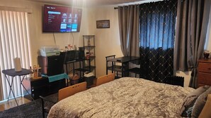 Une chambre d’hôtel avec un lit, un bureau avec un ordinateur, une télévision et une fenêtre avec des rideaux.