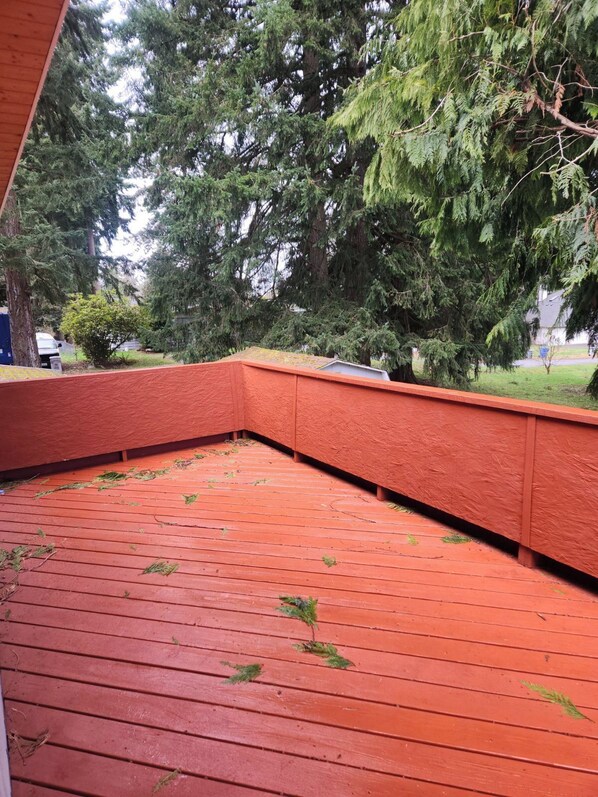 A red wooden deck with a corner bench, surrounded by tall trees.