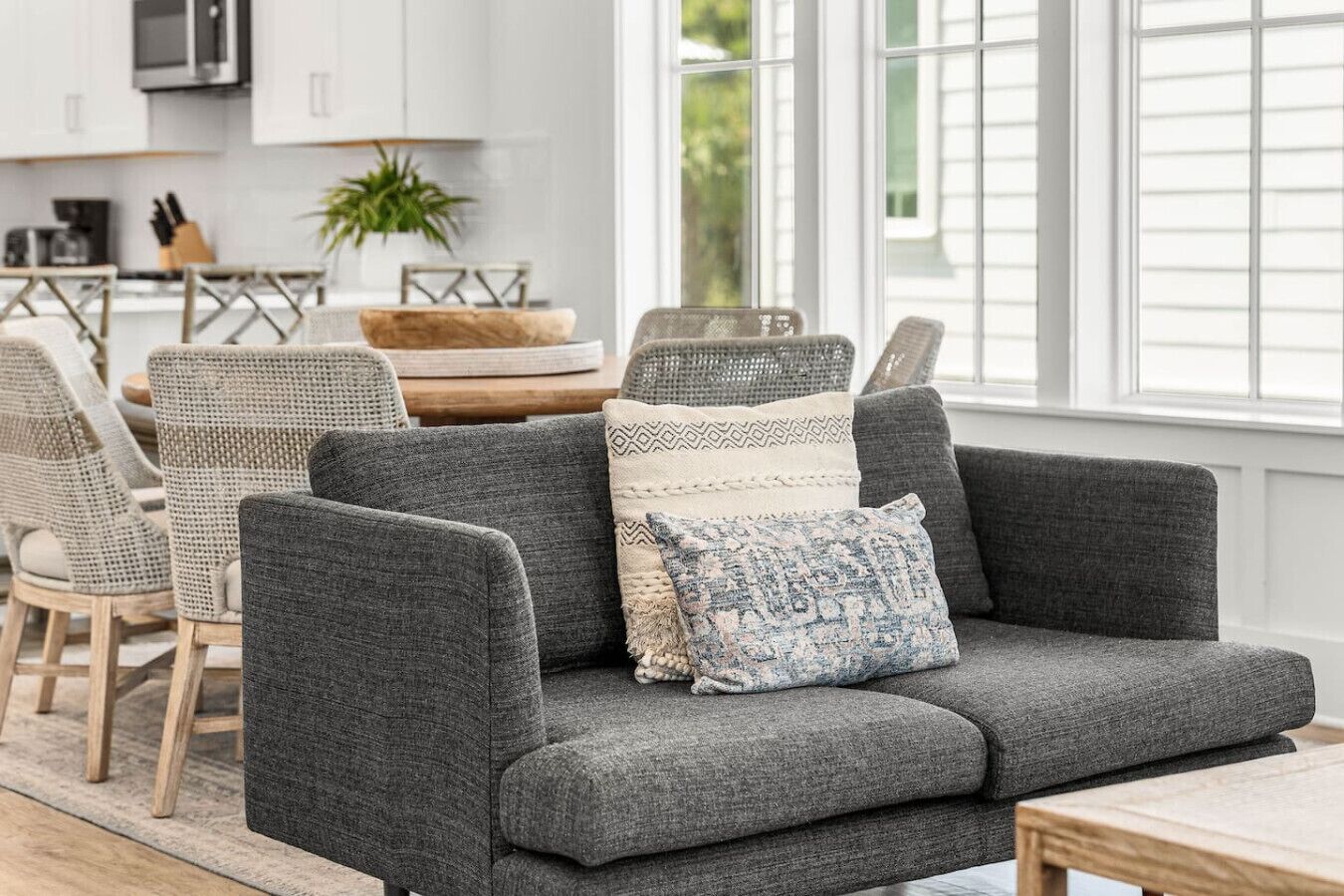 Een moderne woonkamer met een grijze bank, rieten stoelen en een houten salontafel.