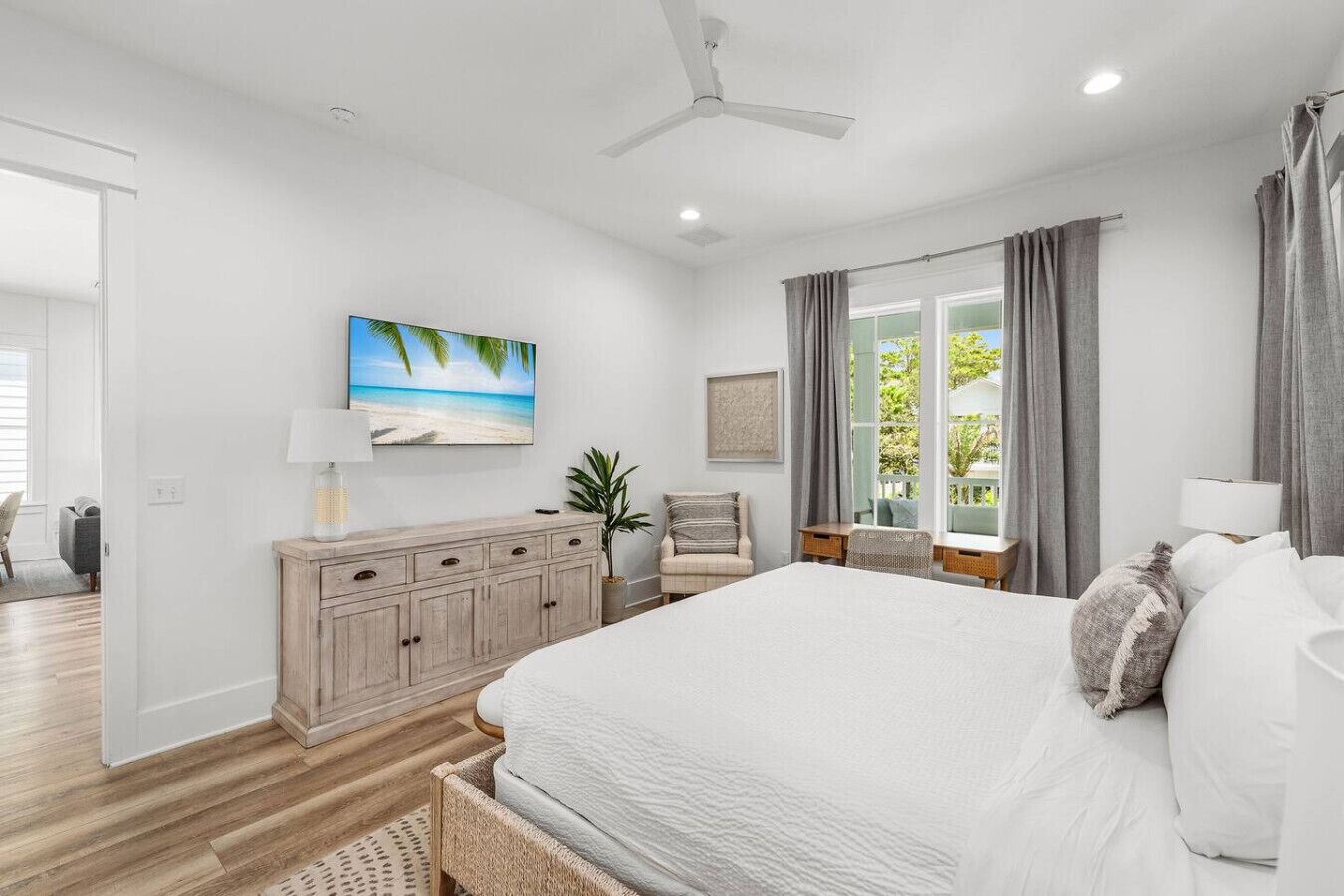 A bedroom with a large bed, a wooden dresser, a desk, a chair, and a window with curtains.