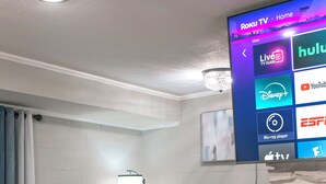 Et moderne soveværelse med en seng, et vægmonteret TV der viser streamingtjenester og en væg med stenudsmykning.