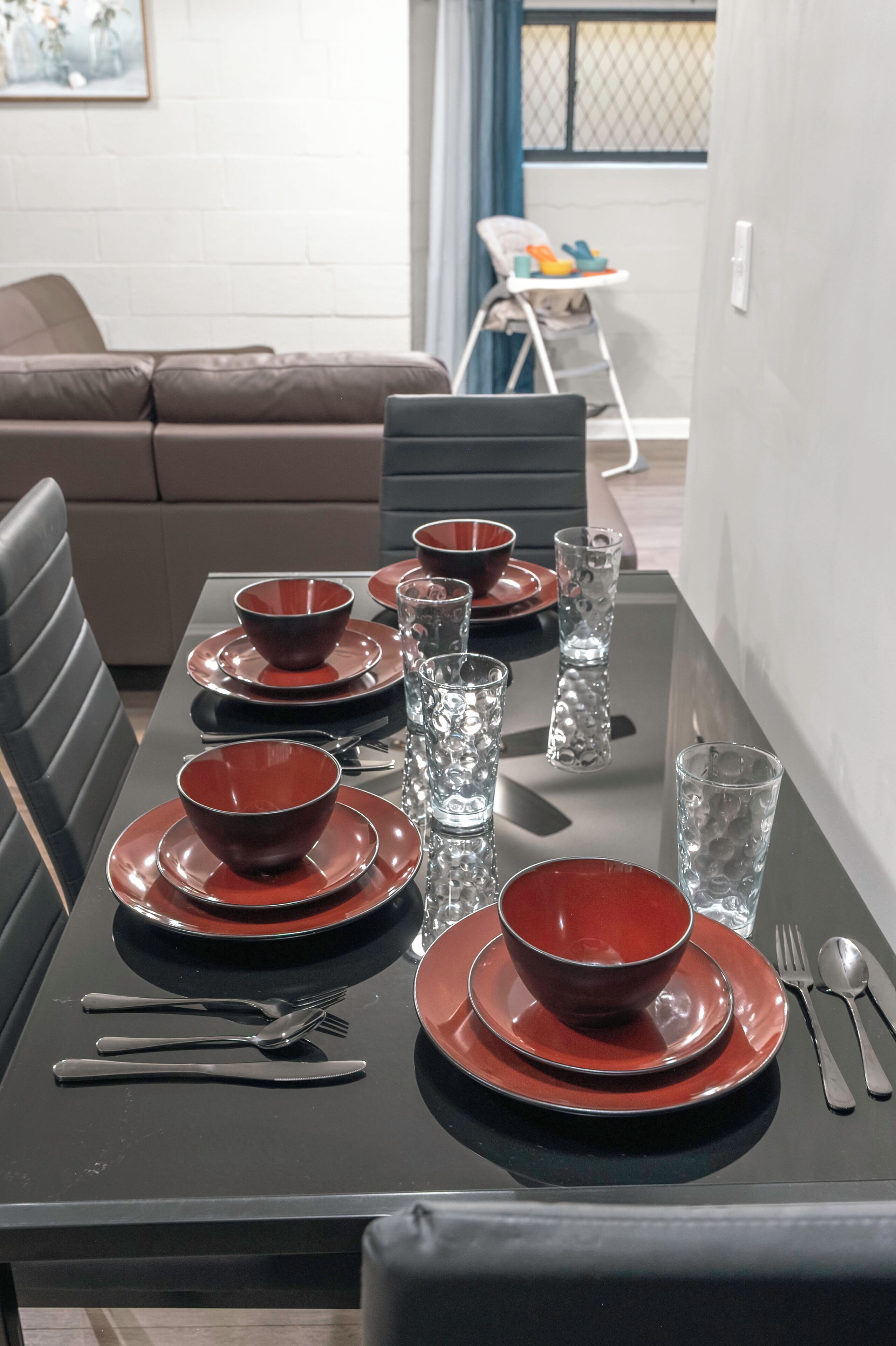 A dining table set with red bowls, plates, and clear glasses, with a black table runner.