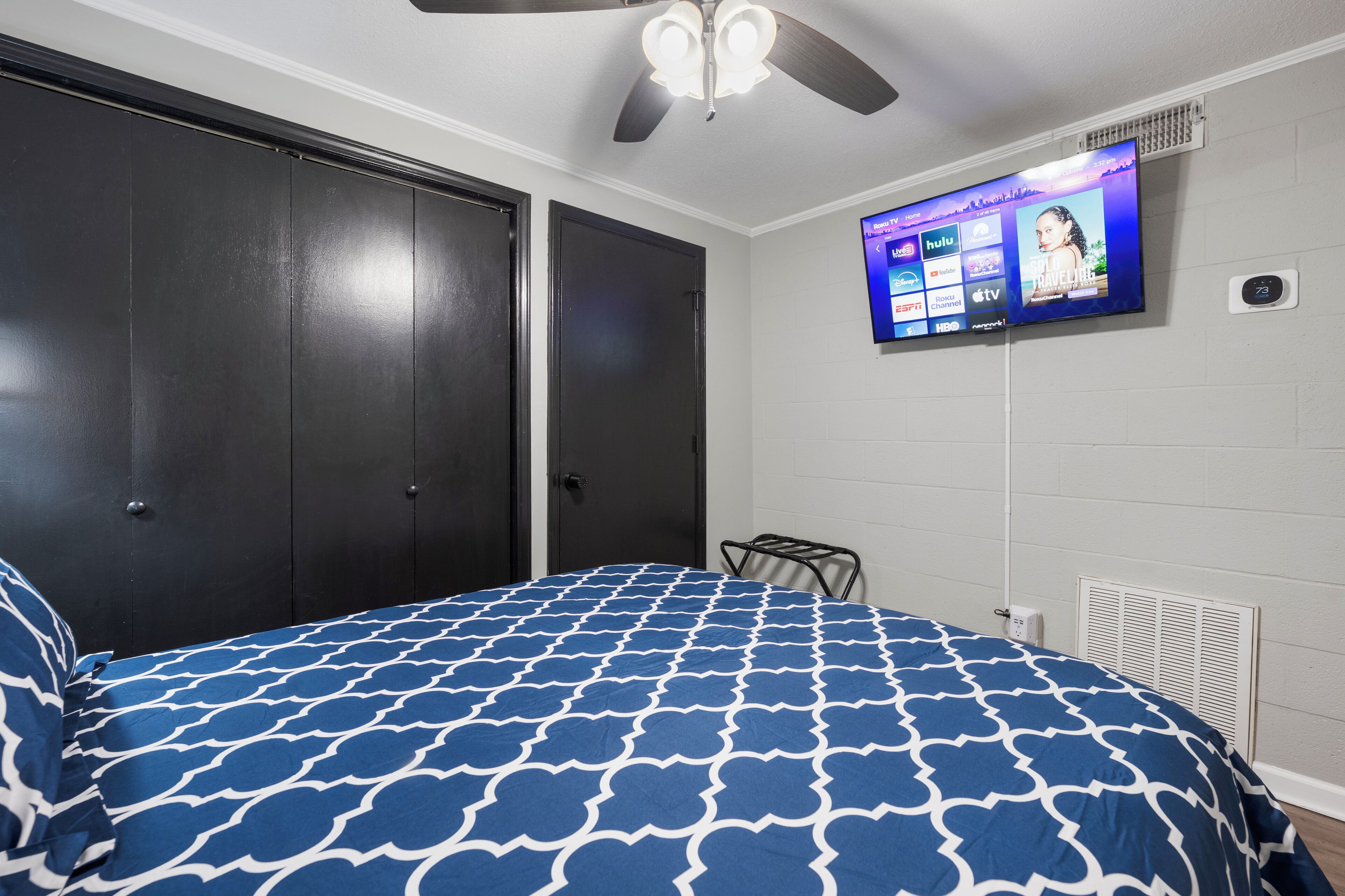 Un dormitorio con una cama, ventilador de techo, televisor montado en la pared y armario.