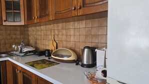 A kitchen with wooden cabinets, a tiled backsplash, a coffee maker, a kettle, and a fruit basket.