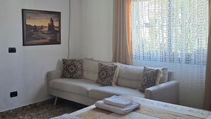 A bedroom with a bed, a sofa, a painting, and a window with curtains.