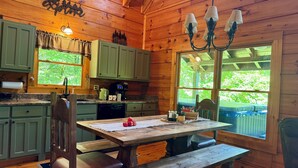 A wooden cabin kitchen with a dining table, benches, and a large window.