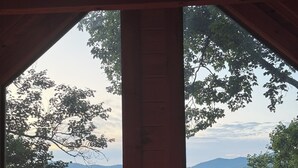 A cabin with a large window offering a view of a forested mountain range.
