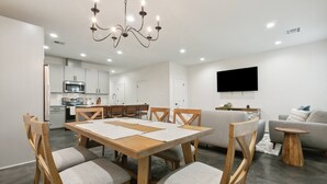 A modern living room with a dining table, chairs, a sofa, a TV, and a kitchen area. - Luxury 3BR in Belle Chasse (Belle Chasse)