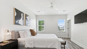 A bedroom with a bed, bedside table, lamp, artwork, windows, and a TV. - Luxury 3BR in Belle Chasse (Belle Chasse)