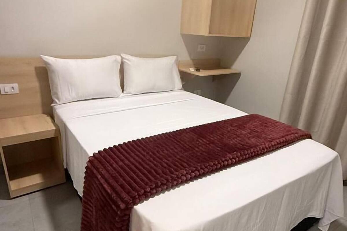 Ein Schlafzimmer mit einem Bett, weißer Bettwäsche, einer roten Decke, einem Nachttisch aus Holz und einer eingebauten Regaleinrichtung.