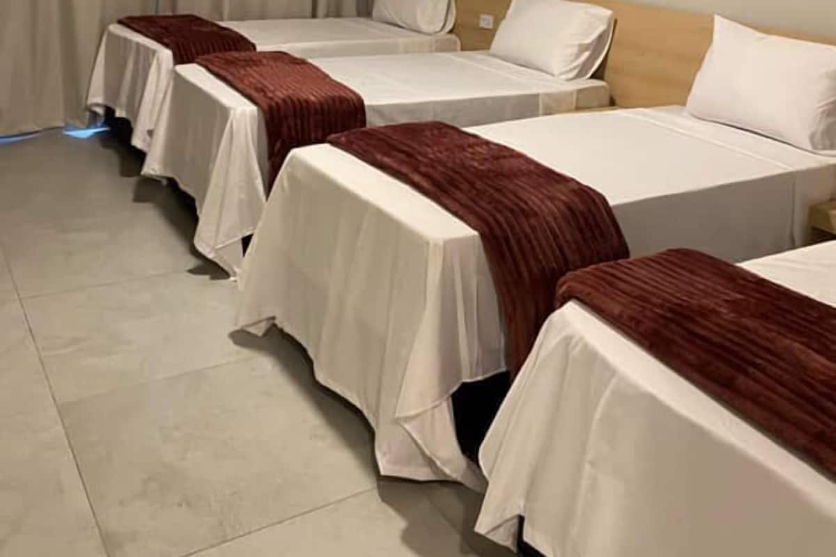 Ein Hotelzimmer mit vier Einzelbetten, die in einer Reihe angeordnet sind, jeweils mit weißer Bettdecke und brauner Decke.