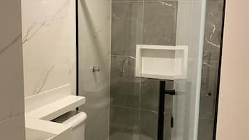 A modern bathroom with a glass-enclosed shower, a white toilet, and a vanity with a mirror.