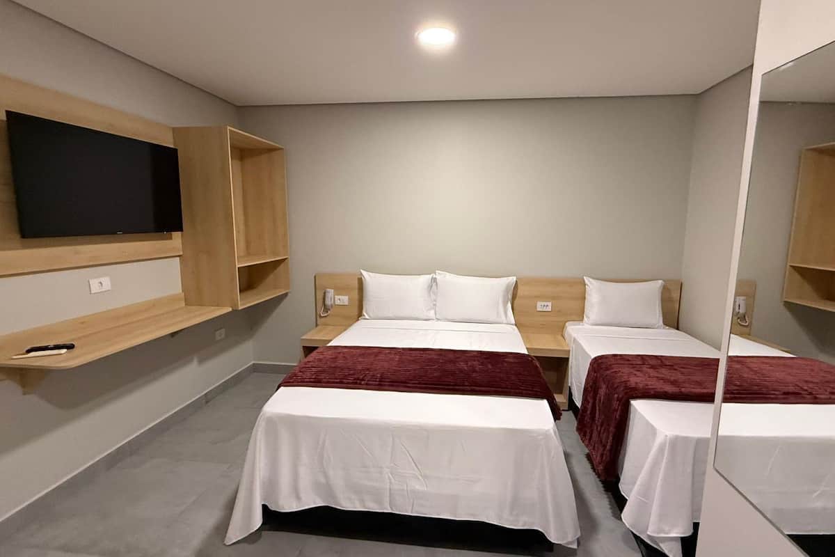 Ein Hotelzimmer mit zwei Betten, einem an der Wand montierten Fernseher und Holzregalen.