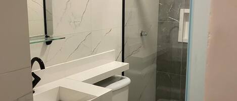 Une salle de bain moderne avec un pare-chocs en marbre blanc, une douche à l’italienne en verre et des toilettes blanches.