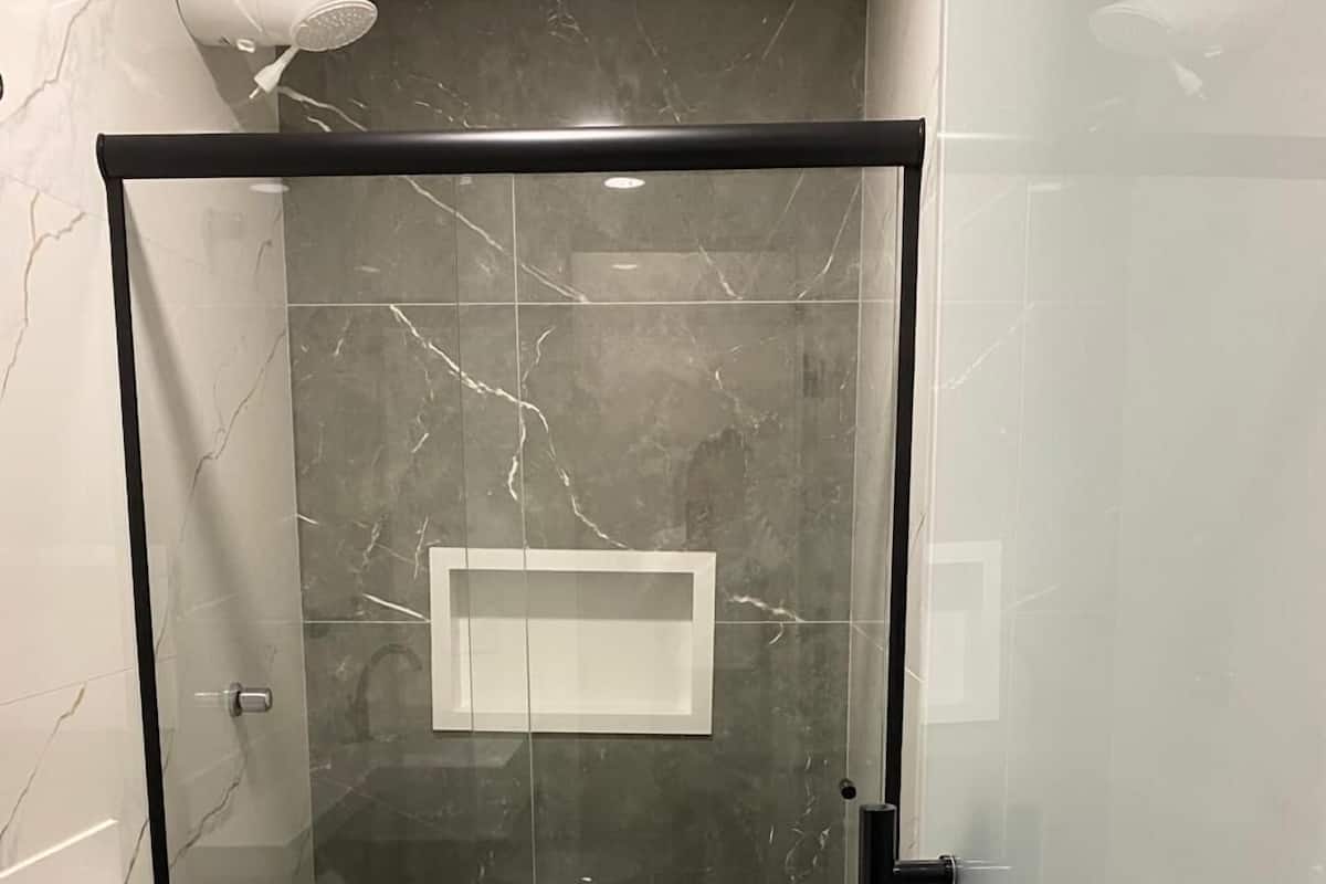 Ein modernes Badezimmer mit einer gläsernen Dusche, einer weißen Toilette und einer marmorverkleideten Wand.