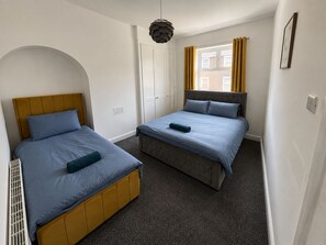 Une chambre avec deux lits, une armoire, une fenêtre avec des rideaux et un luminaire suspendu.