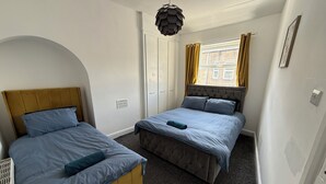 Quarto com duas camas, janela com cortinas, luminária de teto peculiar e porta com ventilação.