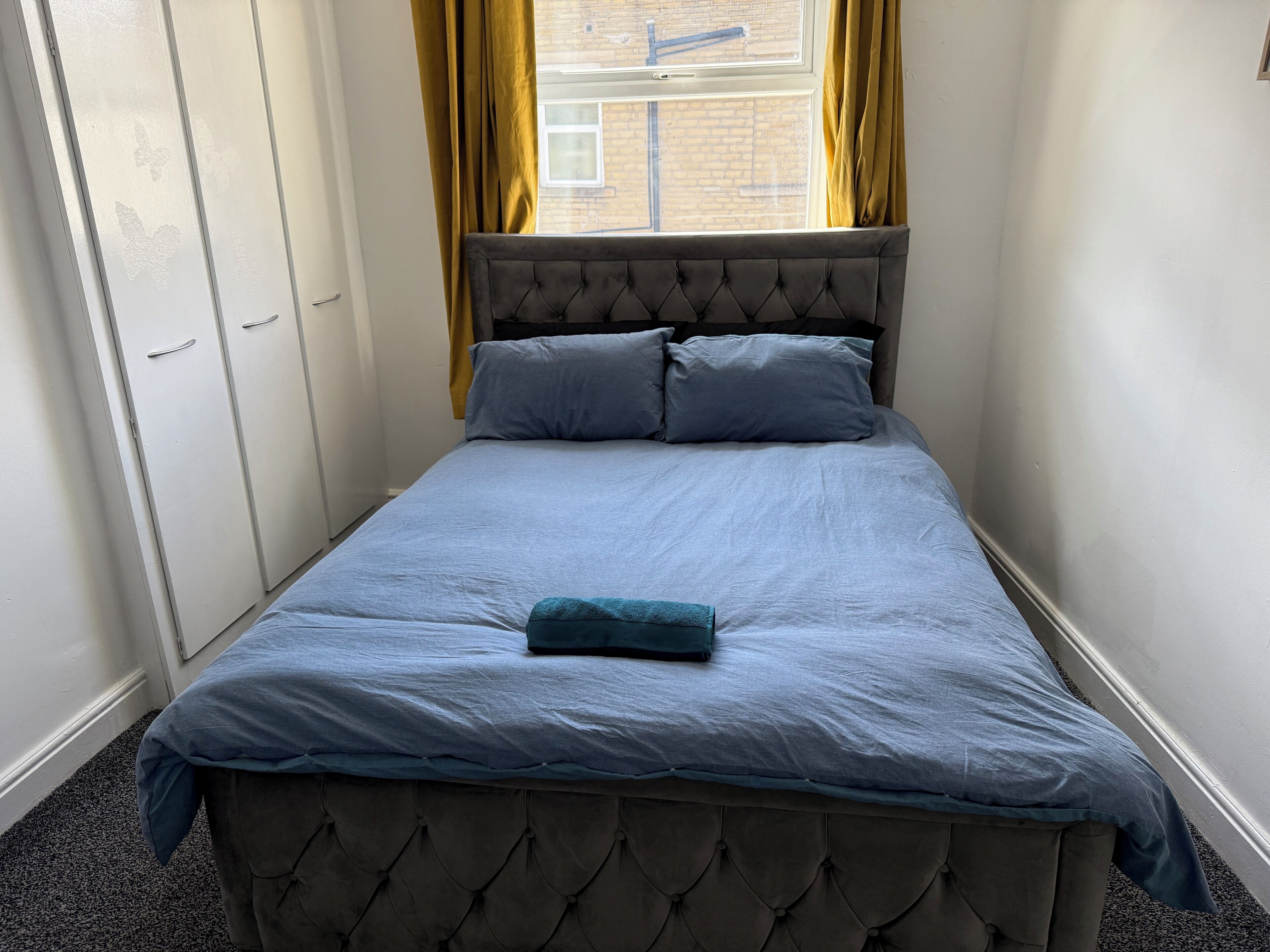 A bedroom with a bed, a wardrobe, and a window with curtains.