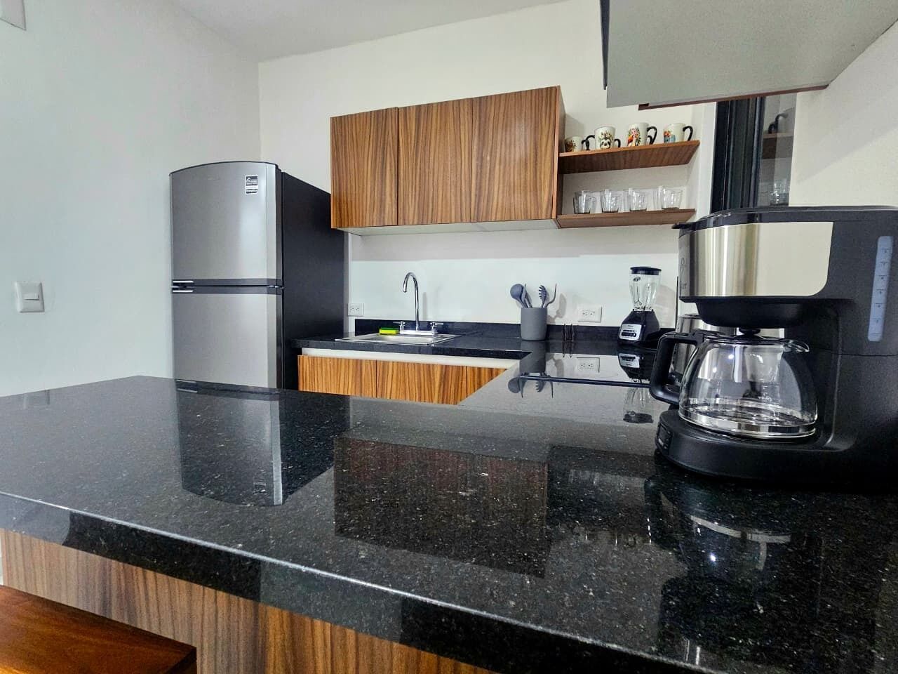Una cocina moderna con encimera de granito negro, electrodomésticos de acero inoxidable, armarios de madera y una cafetera.