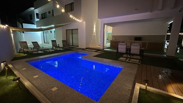 Un área de piscina exterior moderna con sillones de descanso y una zona de bar.