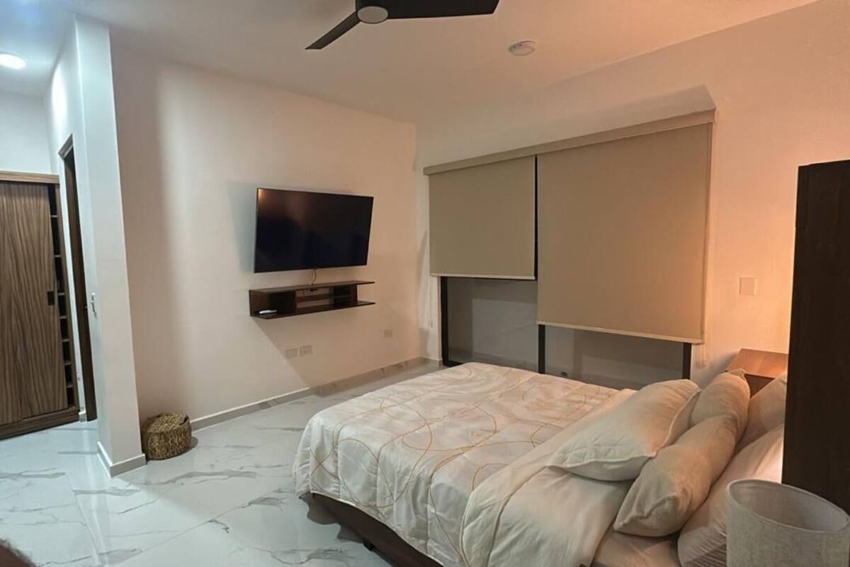 A bedroom with a bed, a TV mounted on the wall, a ceiling fan, and a wardrobe.