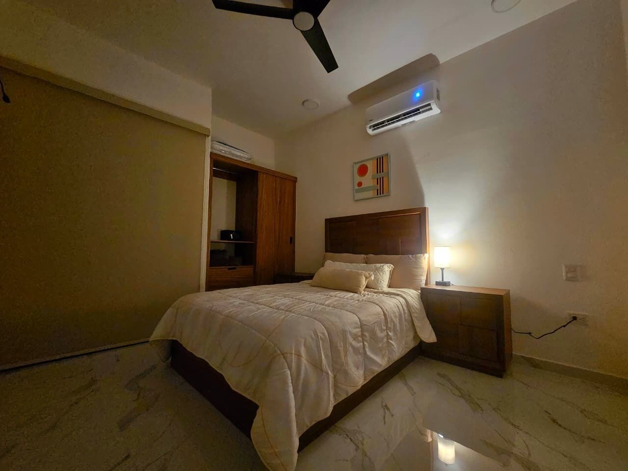 A bedroom with a bed, a nightstand, a ceiling fan, and an air conditioning unit.