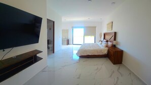 Habitación de hotel moderna con una televisión de pantalla plana grande montada en la pared, una cama con cabecera de madera y un ventanal con vistas al exterior.