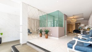 Un vestíbulo moderno con suelo de mármol, un separador de vidrio y una zona de estar con sillones tapizados en azul.