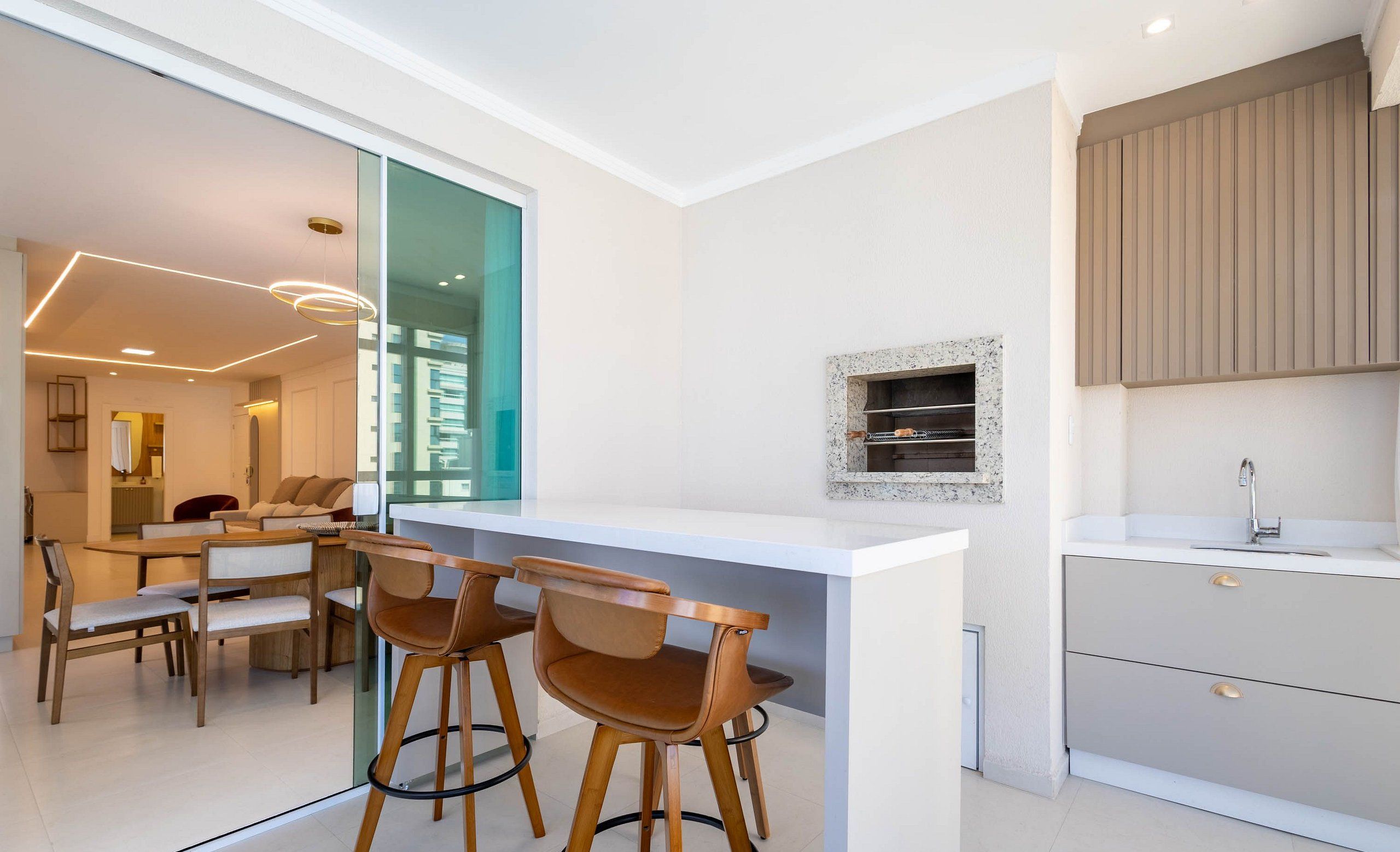 Una cocina moderna con encimera blanca, taburetes de madera y horno empotrado.