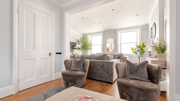 A spacious living room with a large grey sofa set, a coffee table with a decorative item, and a wooden floor.