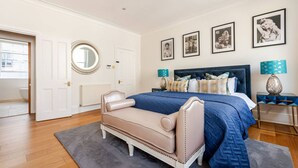 A bedroom with a large bed, a round mirror, a beige sofa, and a blue bedspread.